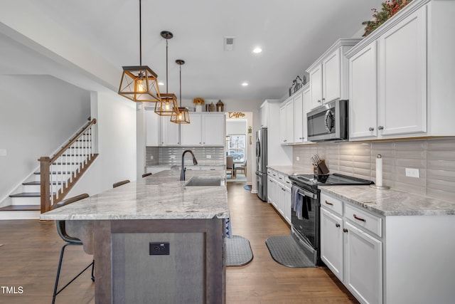 kitchen with stainless steel appliances, a breakfast bar, a sink, white cabinetry, and dark wood finished floors