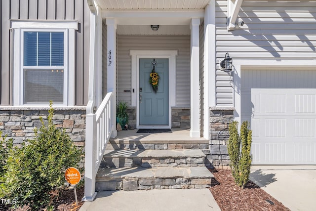 entrance to property with board and batten siding, stone siding, covered porch, and a garage