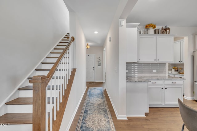 interior space featuring light wood-style floors, white cabinetry, backsplash, and light stone counters