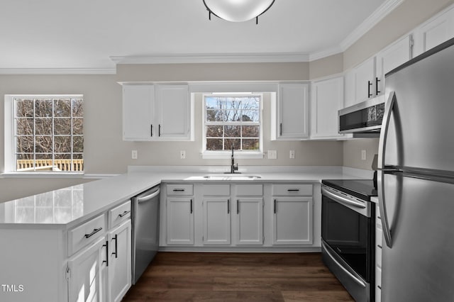 kitchen featuring appliances with stainless steel finishes, a peninsula, light countertops, white cabinetry, and a sink