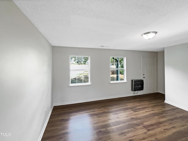 empty room featuring a textured ceiling, dark wood-style flooring, and heating unit