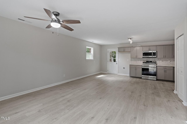 kitchen with light wood-style flooring, gray cabinetry, stainless steel appliances, light countertops, and decorative backsplash