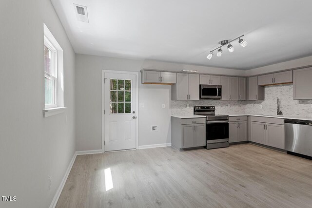 kitchen with tasteful backsplash, light countertops, gray cabinetry, appliances with stainless steel finishes, and a sink