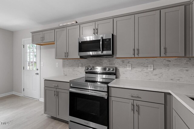 kitchen with stainless steel appliances, gray cabinets, light countertops, and light wood-style floors