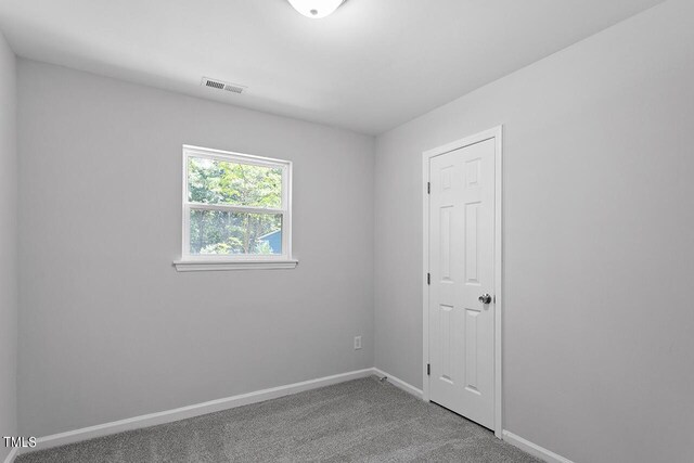 unfurnished room with carpet, visible vents, and baseboards