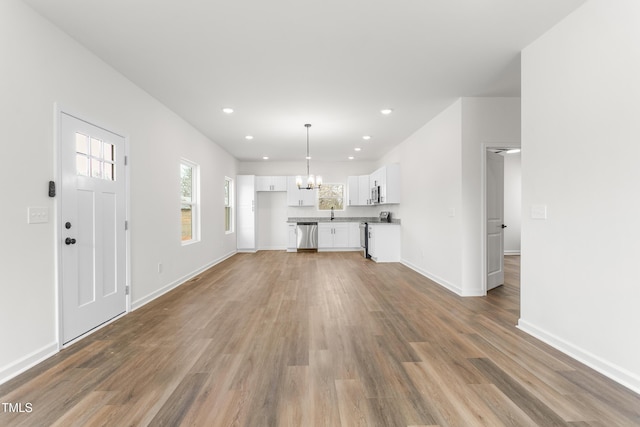 unfurnished living room featuring recessed lighting, an inviting chandelier, a sink, wood finished floors, and baseboards