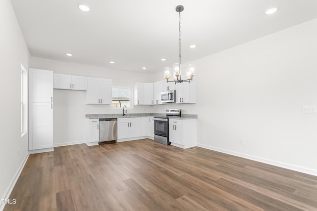 kitchen with hanging light fixtures, white cabinets, stainless steel appliances, and wood finished floors