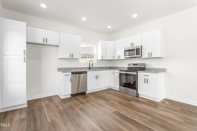 kitchen featuring dark wood finished floors, white cabinets, appliances with stainless steel finishes, light stone counters, and a sink