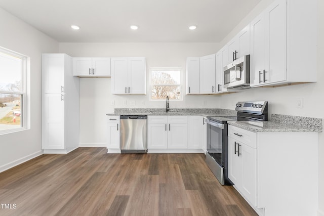 kitchen with white cabinets, dark wood finished floors, light stone countertops, stainless steel appliances, and a sink