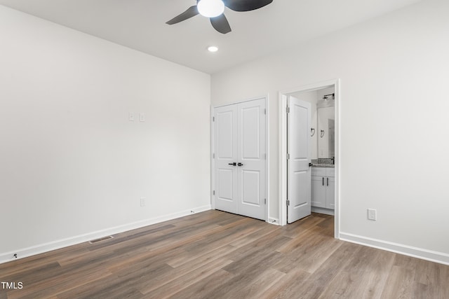 unfurnished bedroom with ensuite bathroom, wood finished floors, visible vents, and baseboards