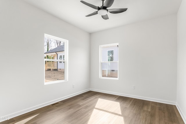 unfurnished room with plenty of natural light, wood finished floors, visible vents, and baseboards