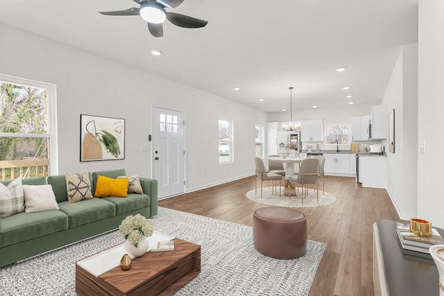 living room with ceiling fan with notable chandelier, light wood finished floors, baseboards, and recessed lighting