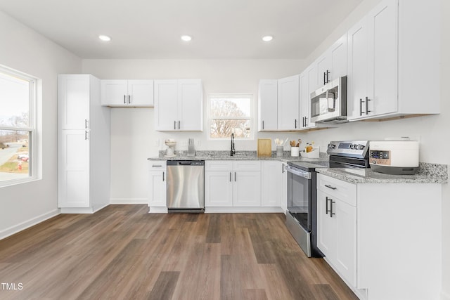 kitchen featuring light stone counters, stainless steel appliances, dark wood-type flooring, white cabinetry, and a sink