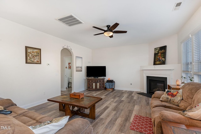 living area with visible vents, arched walkways, baseboards, a glass covered fireplace, and light wood-style flooring