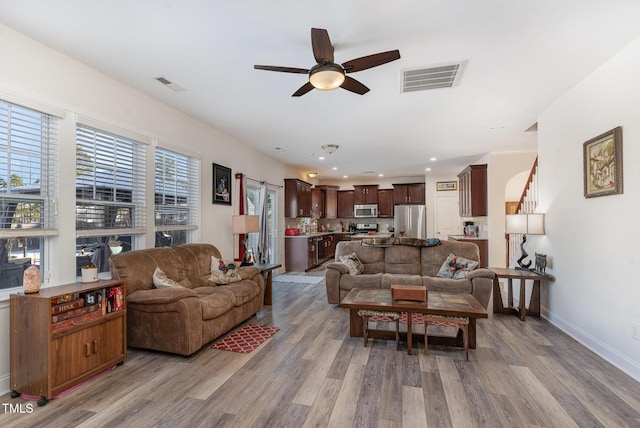 living room with baseboards, visible vents, ceiling fan, and light wood finished floors