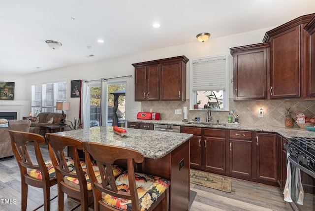 kitchen with a center island, light wood finished floors, open floor plan, a sink, and light stone countertops