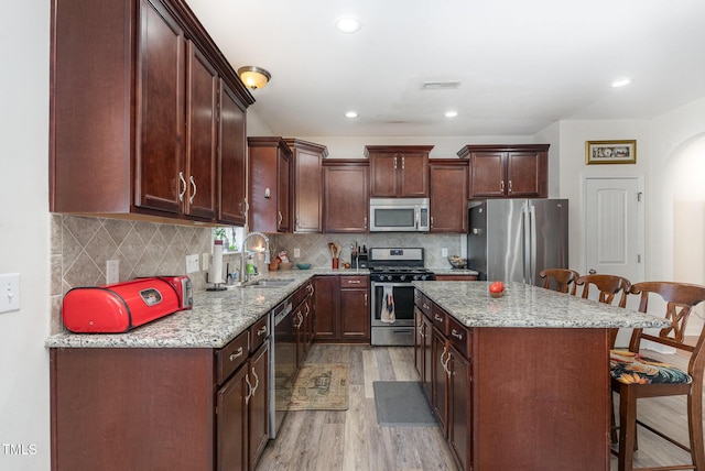 kitchen with light stone counters, a sink, a kitchen island, a kitchen breakfast bar, and appliances with stainless steel finishes