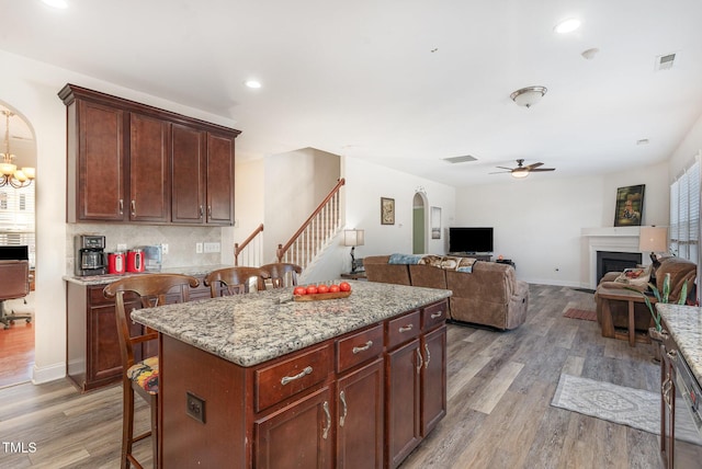 kitchen with arched walkways, a breakfast bar, open floor plan, wood finished floors, and a center island