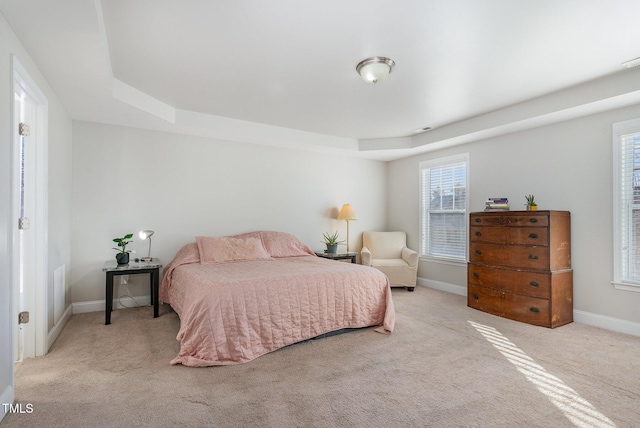 bedroom with multiple windows, light carpet, and baseboards