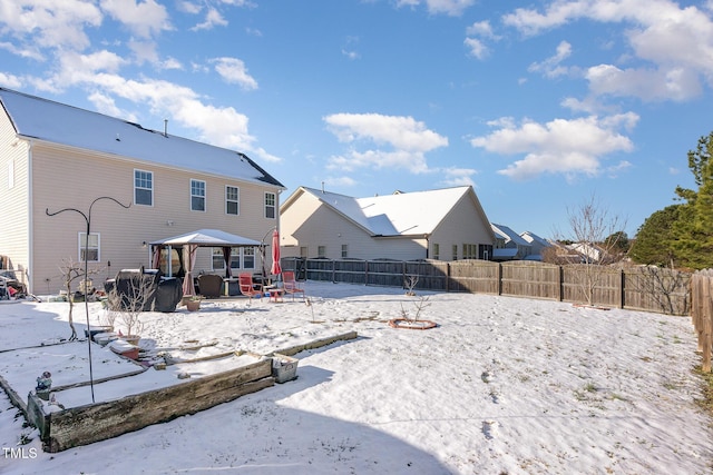 snow covered back of property with a fenced backyard and a gazebo