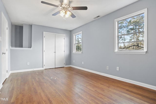 unfurnished bedroom featuring baseboards, visible vents, a ceiling fan, wood finished floors, and a closet