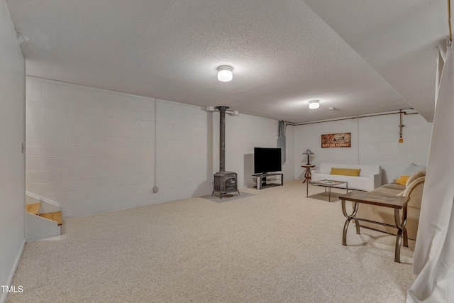 interior space with a textured ceiling, carpet flooring, a wood stove, and concrete block wall