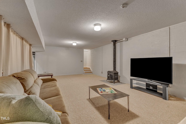 carpeted living room featuring concrete block wall, a wood stove, stairway, and a textured ceiling