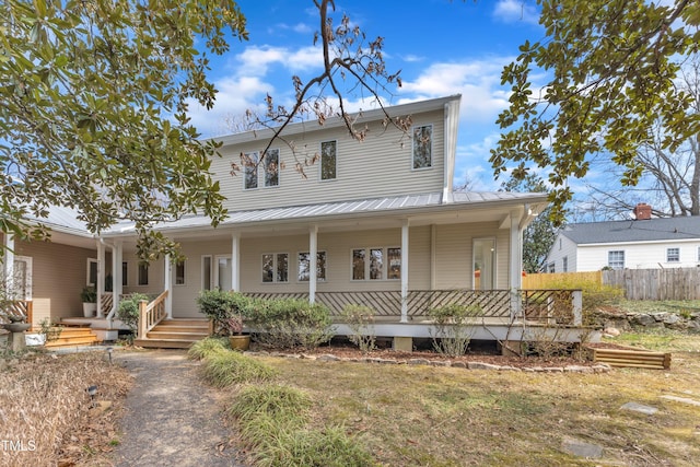 farmhouse-style home with a porch, metal roof, and fence