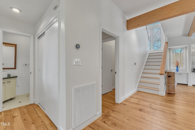 corridor with light wood-style flooring, visible vents, baseboards, stairs, and beamed ceiling