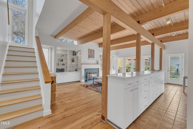 kitchen featuring wood ceiling, white cabinetry, open floor plan, light wood finished floors, and a glass covered fireplace