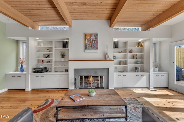 living room with light wood finished floors, a glass covered fireplace, wood ceiling, beamed ceiling, and built in shelves