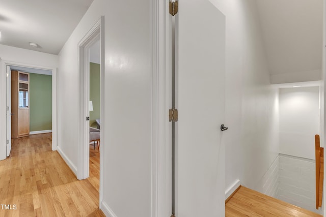 hall featuring light wood-style flooring, baseboards, and an upstairs landing