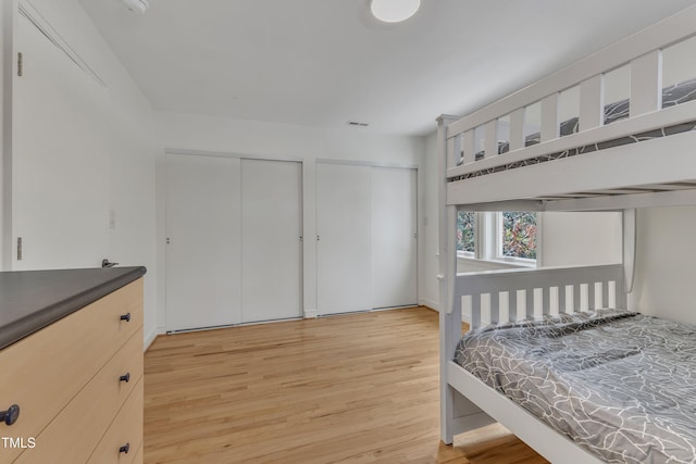 bedroom with visible vents, light wood-style flooring, and two closets