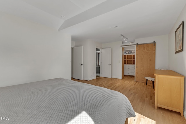 bedroom featuring light wood-style floors, track lighting, baseboards, and a barn door