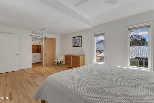 bedroom featuring a barn door, visible vents, ceiling fan, light wood-style flooring, and track lighting