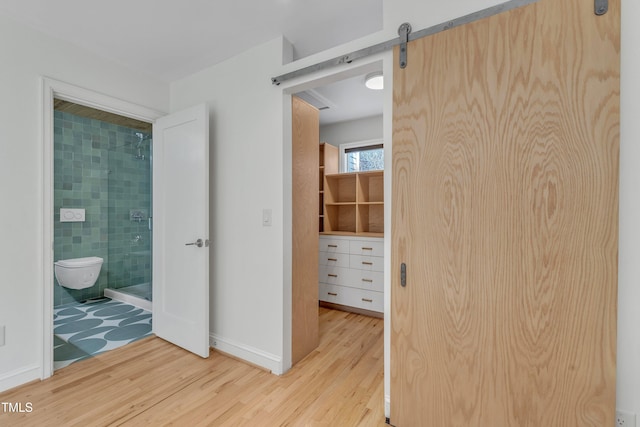 interior space with a barn door, baseboards, wood finished floors, and ensuite bathroom