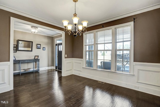 unfurnished dining area with crown molding, visible vents, an inviting chandelier, dark wood-type flooring, and wainscoting