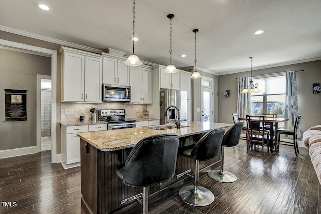 kitchen with an island with sink, light stone countertops, stainless steel appliances, crown molding, and white cabinetry