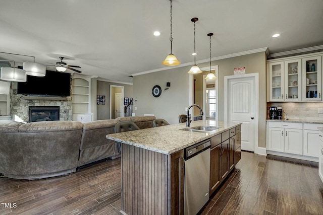 kitchen with dishwasher, open floor plan, light stone countertops, a kitchen island with sink, and a sink