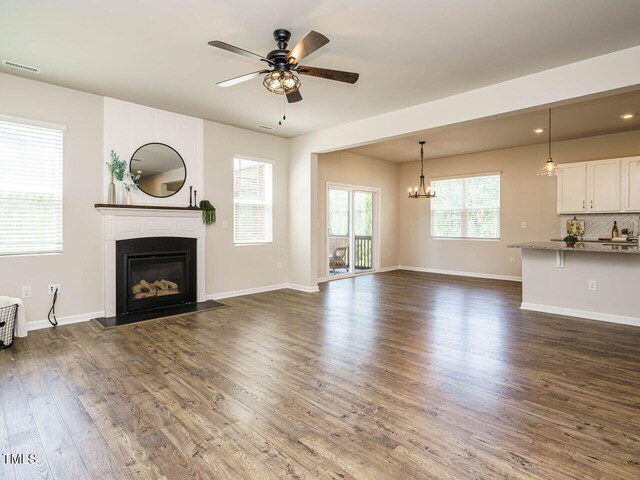 unfurnished living room featuring a chandelier, dark wood-style flooring, a glass covered fireplace, a ceiling fan, and baseboards