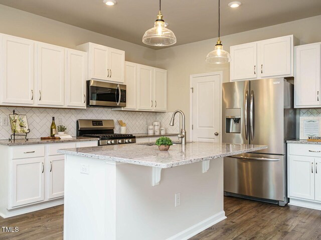 kitchen with appliances with stainless steel finishes, a sink, backsplash, light stone counters, and white cabinets