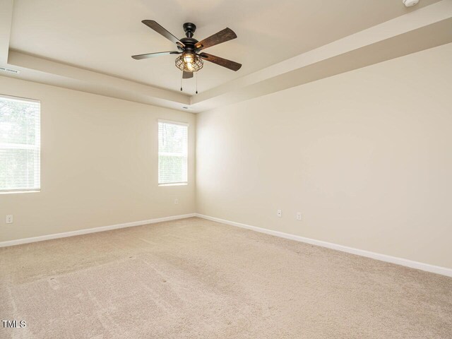 carpeted empty room with baseboards, a tray ceiling, a ceiling fan, and a smoke detector