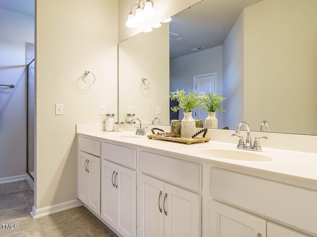 bathroom with double vanity, tile patterned floors, baseboards, and a shower with door