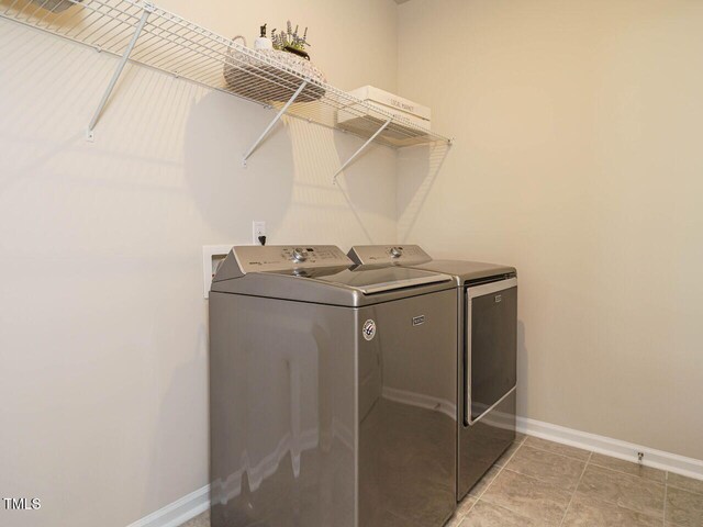 clothes washing area with washer and clothes dryer, baseboards, and light tile patterned floors