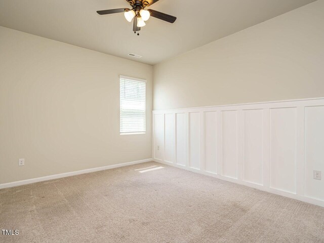 carpeted empty room with ceiling fan, a wainscoted wall, and a decorative wall