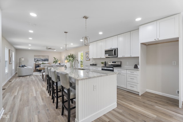 kitchen with recessed lighting, a sink, stainless steel appliances, white cabinets, and a kitchen breakfast bar