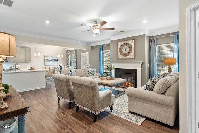 living area with visible vents, ornamental molding, wood finished floors, and a glass covered fireplace