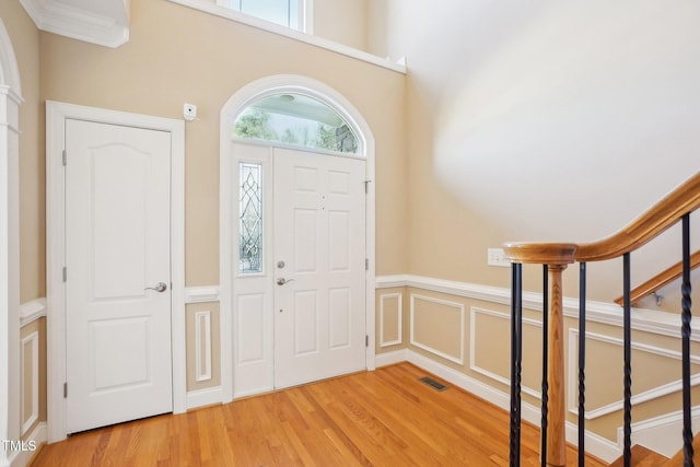 foyer featuring visible vents, stairs, wainscoting, wood finished floors, and a decorative wall