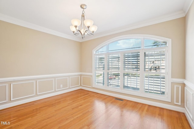 empty room featuring visible vents, an inviting chandelier, wood finished floors, and crown molding