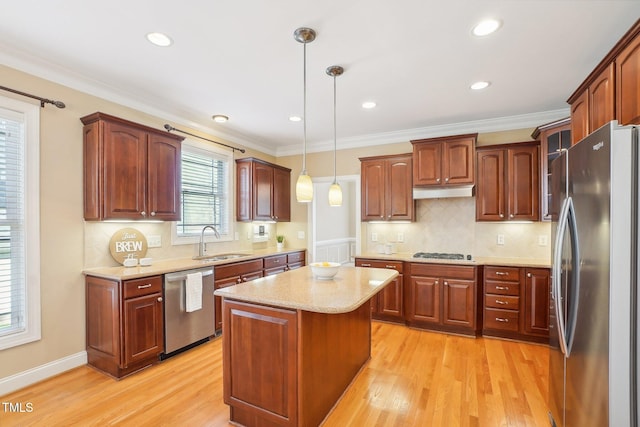 kitchen featuring under cabinet range hood, pendant lighting, light wood-type flooring, appliances with stainless steel finishes, and a sink